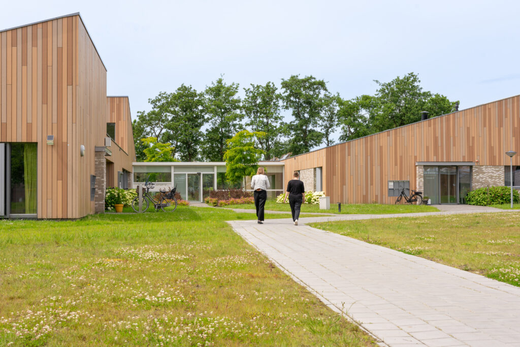 Twee vrouwen lopen op een voetpad naar twee houten gebouwen