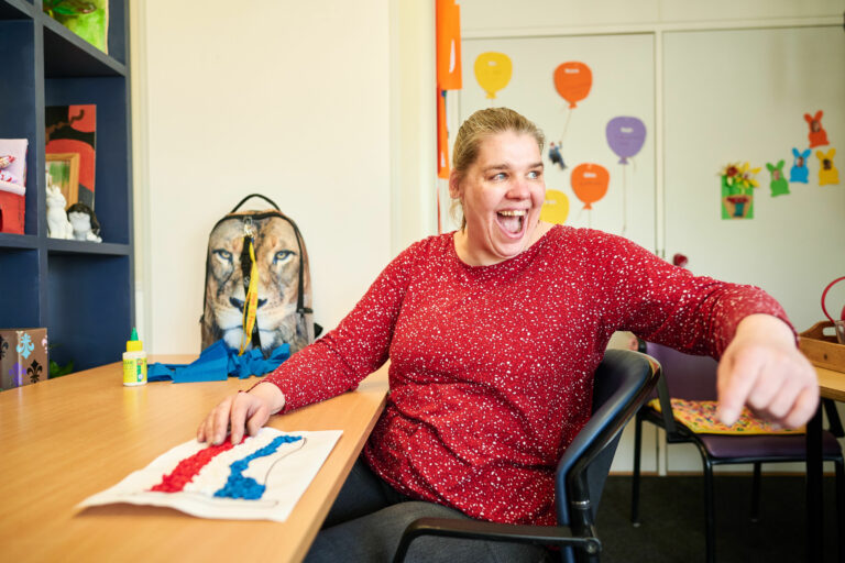 Vrolijk lachende vrouw in rood shirt zit te knutselen