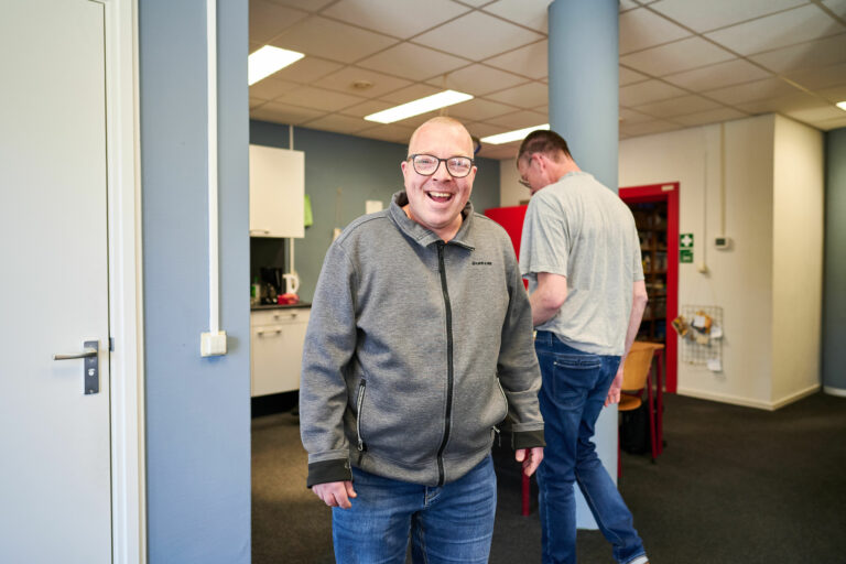 Man in grijs vest staat lachend in een keuken