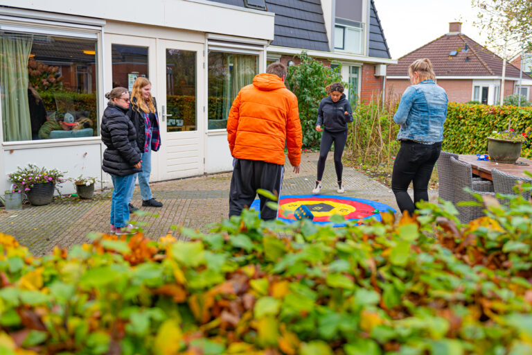 Vijf personen staan in een cirkel om gekleurde ringen op de grond