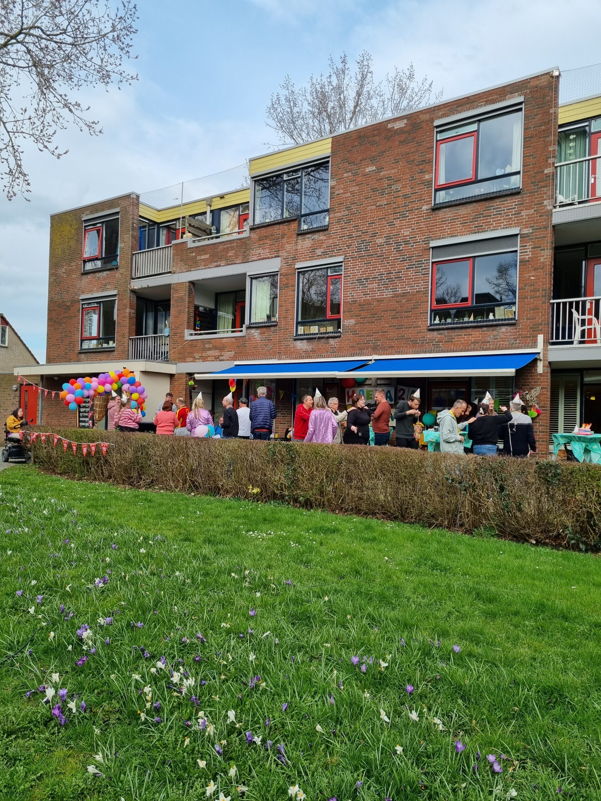 Veel personen sommige met feesthoedjes op voor een flatgebouw