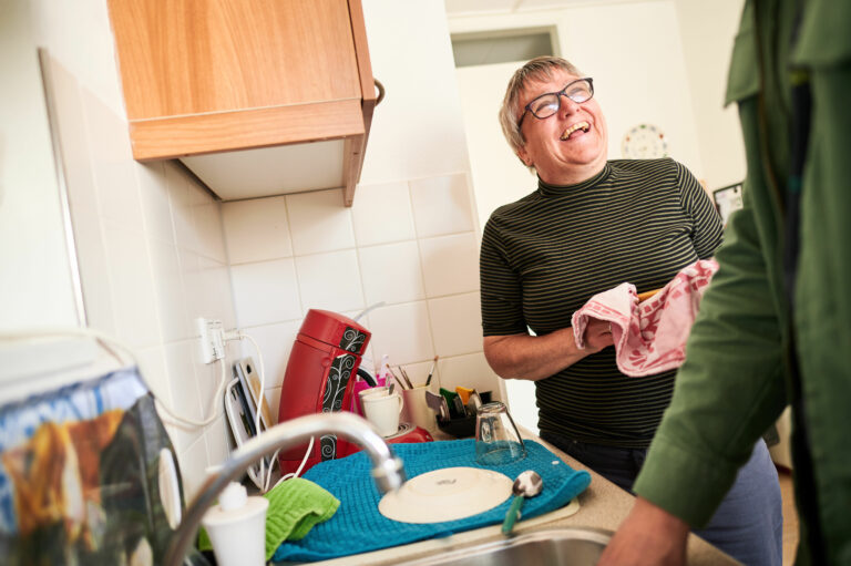 Vrolijk lachende vrouw staat in de keuken af te drogen