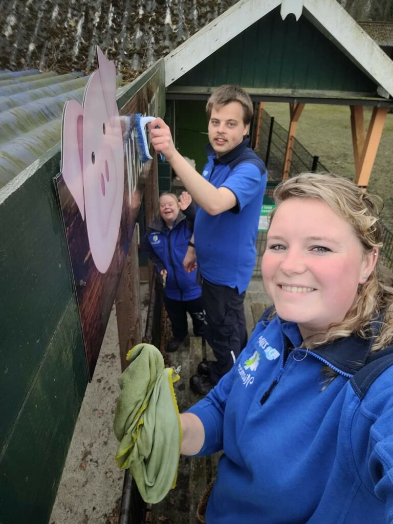 Drie personen in werkkleding maken houten bord bij attractie schoon