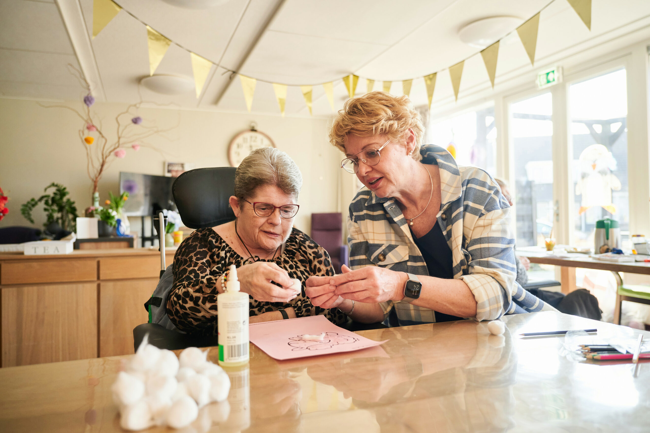 Twee vrouwen aan tafel die samen aan het knutselen zijn met lijm en watjes