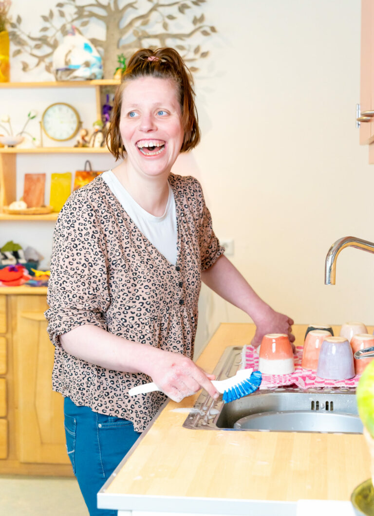 Jonge vrouw staat lachend de afwas te doen