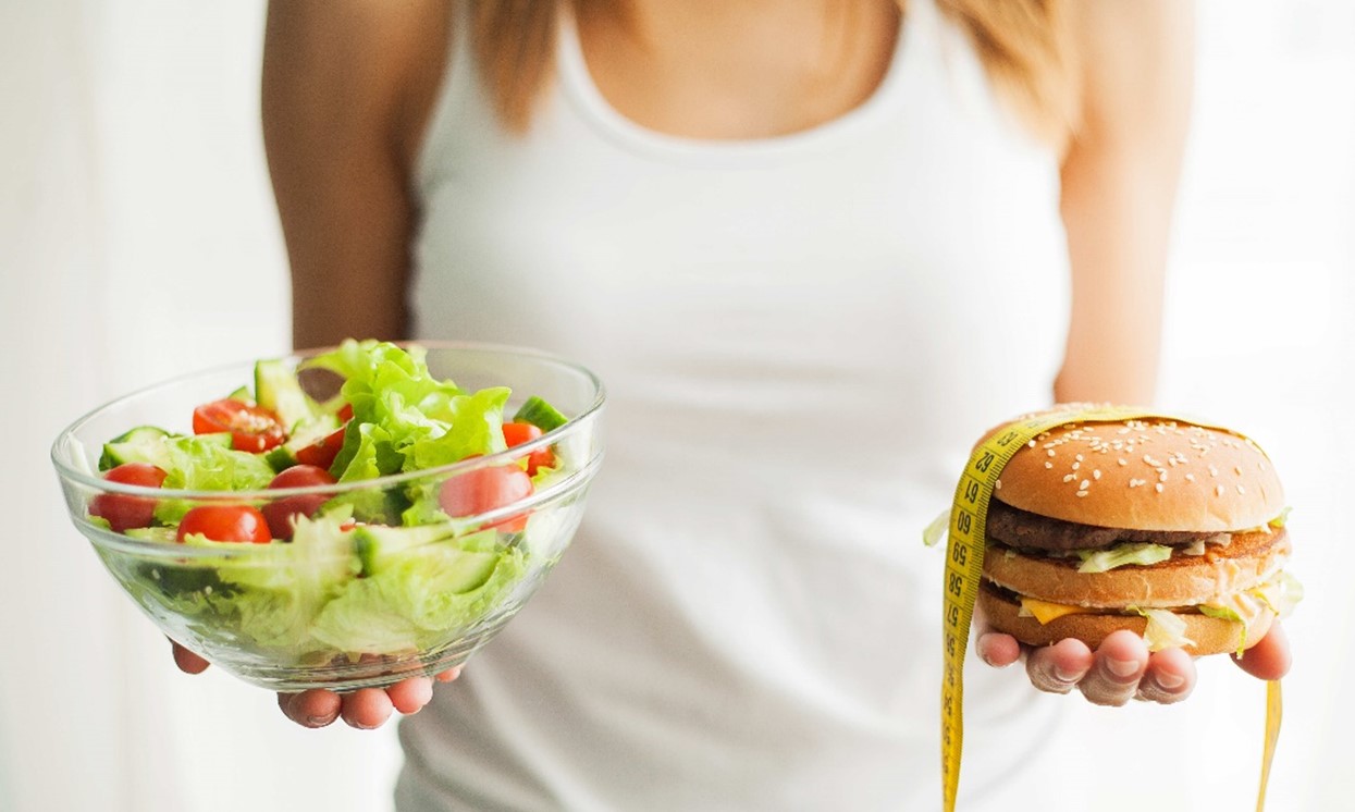 Vrouw met in haar ene hand een gezonde salade en in de andere een broodje hamburger