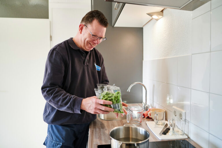 Jonge vrolijk kijkende man doet sperziebonen in een pan