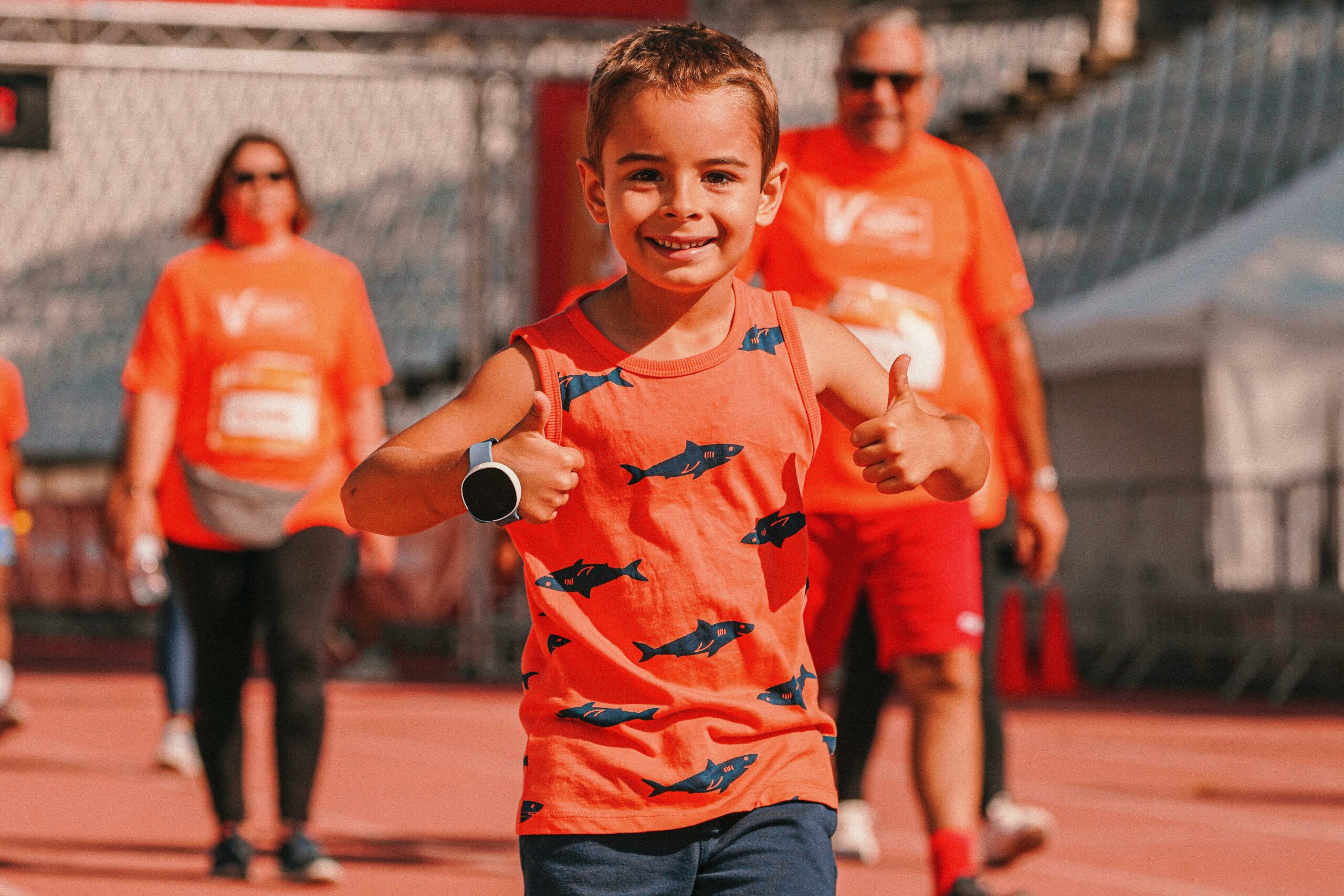 jongen in oranje shirt duimen omhoog vrouw en man lopen erachter