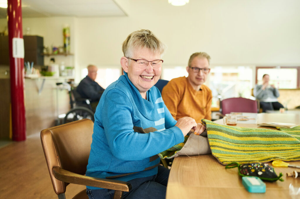 Vrouw zit aan tafel te handwerken man zit erbij thee te drinken