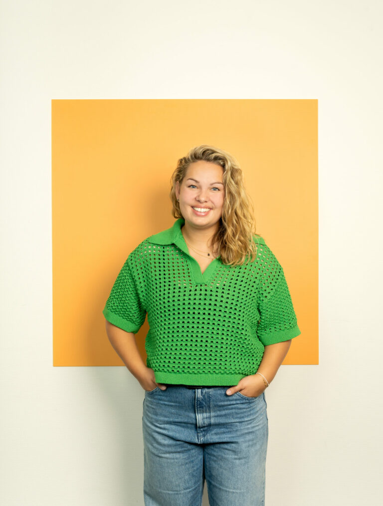 Lachende jonge vouw met lang krullend haar en groene trui staat voor licht oranje vierkant