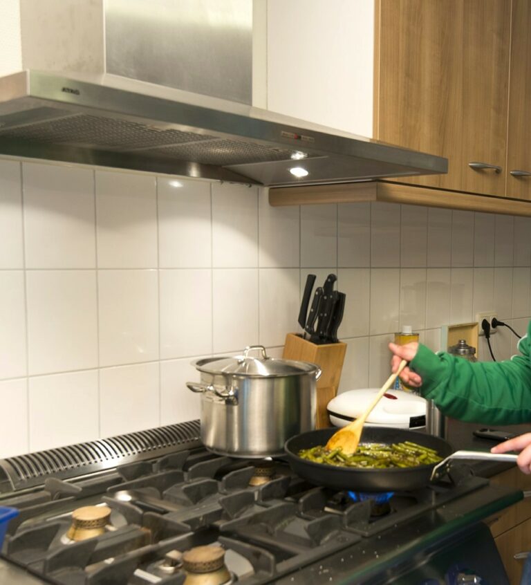 Iemand in een groene trui roert in een koekenpan.