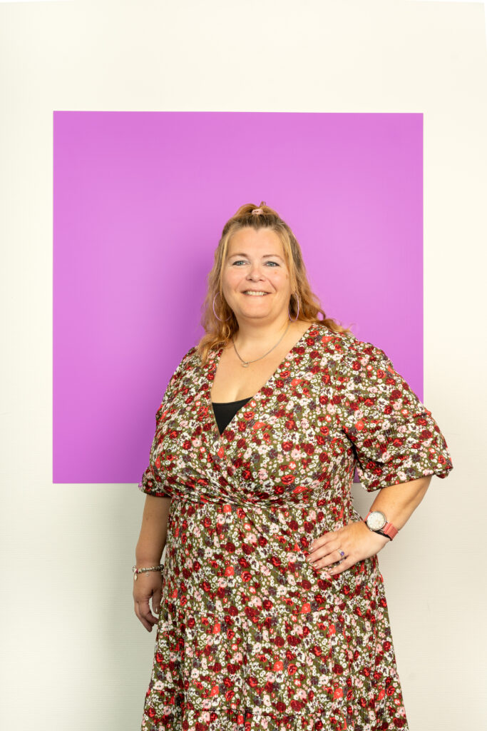 Vrolijke vrouw in bloemetjesjurk staand voor een roze vierkant