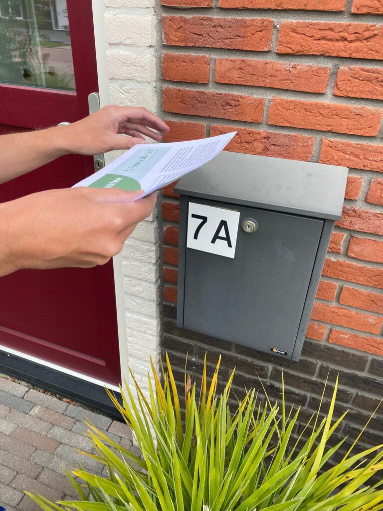 Brievenbus naast rode voordeur met nummer 7A iemand doet er een foldertje in