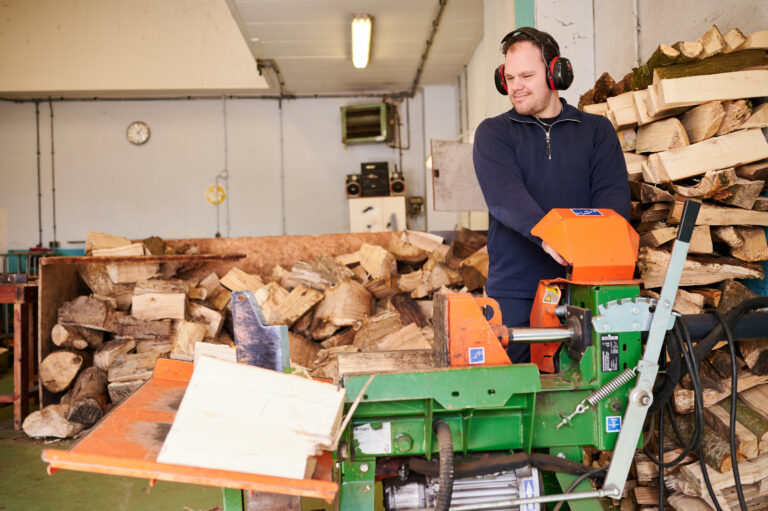 Jonge man met gehoorbescherming tussen stukken hout en een kloofmachine