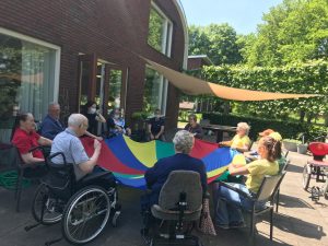 Veel mensen in stoelen of roelstoelen houden een gekleurd doek vast