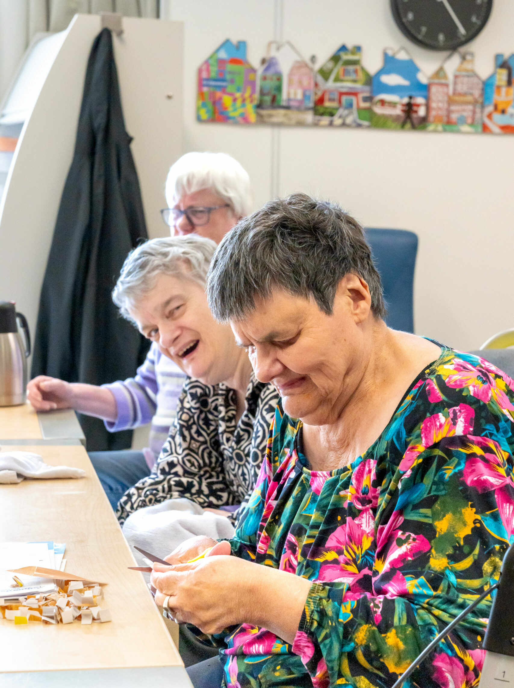 Drie oudere vrouwen zitten aan een tafel figuurtjes uit te knippen