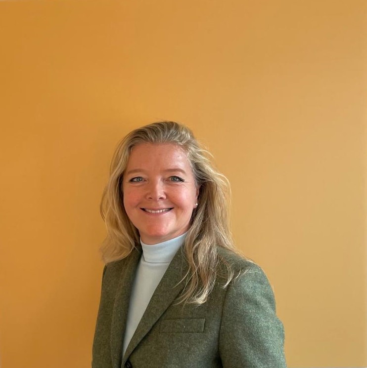 Vrolijk lachende vrouw met lang blond haar en groen colbertje voor geel vierkant