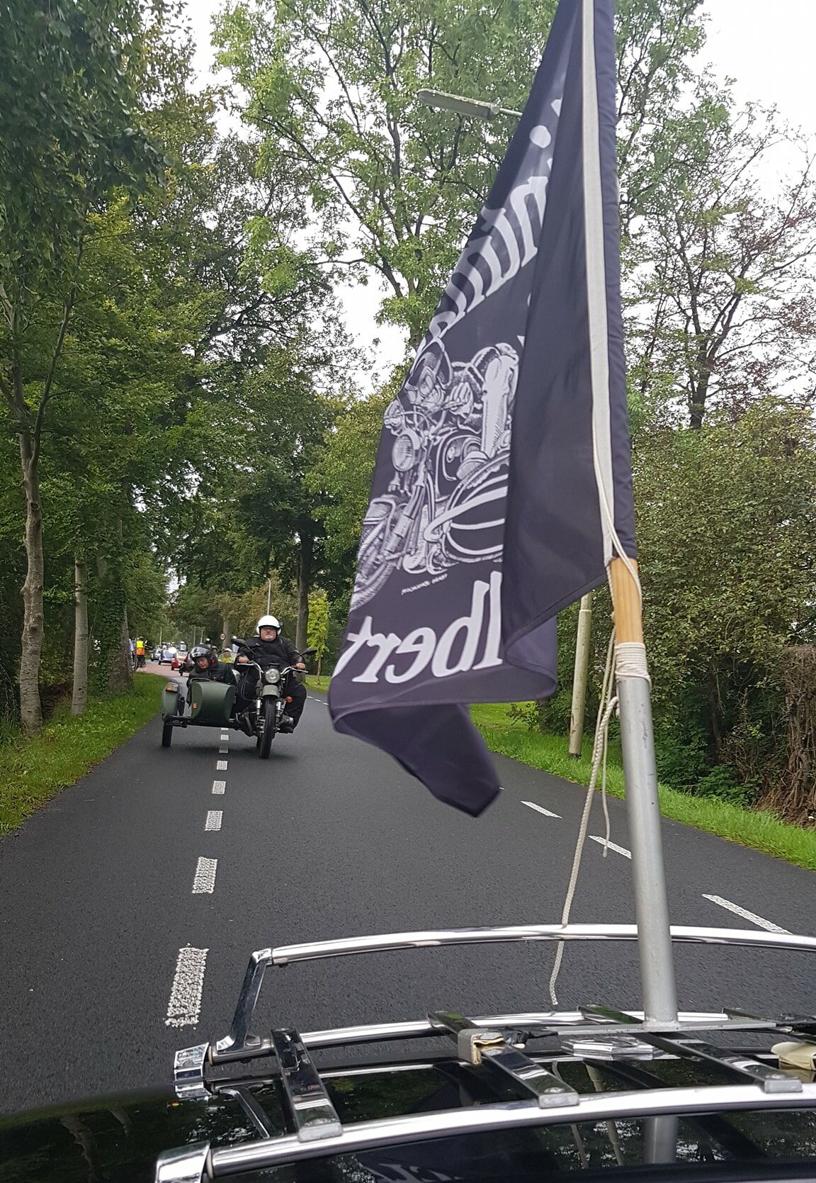 Motor chauffeur en iemand in zijspan rijdt achter een andere motor aan met vlag erop